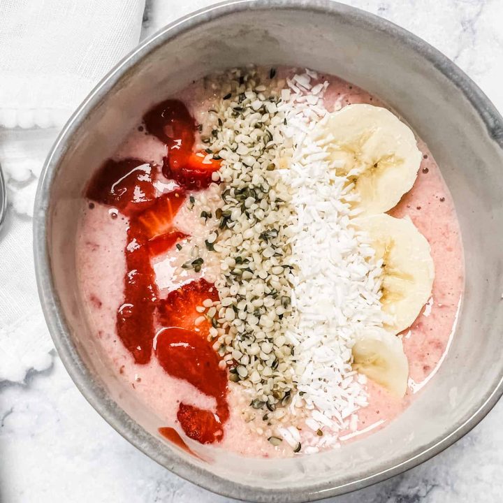 strawberry and banana slices along with hemp seeds and coconut top a bowl of strawberry banana yogurt